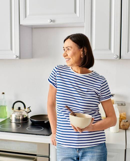 Mature woman in cozy homewear holding a bowl in her kitchen.